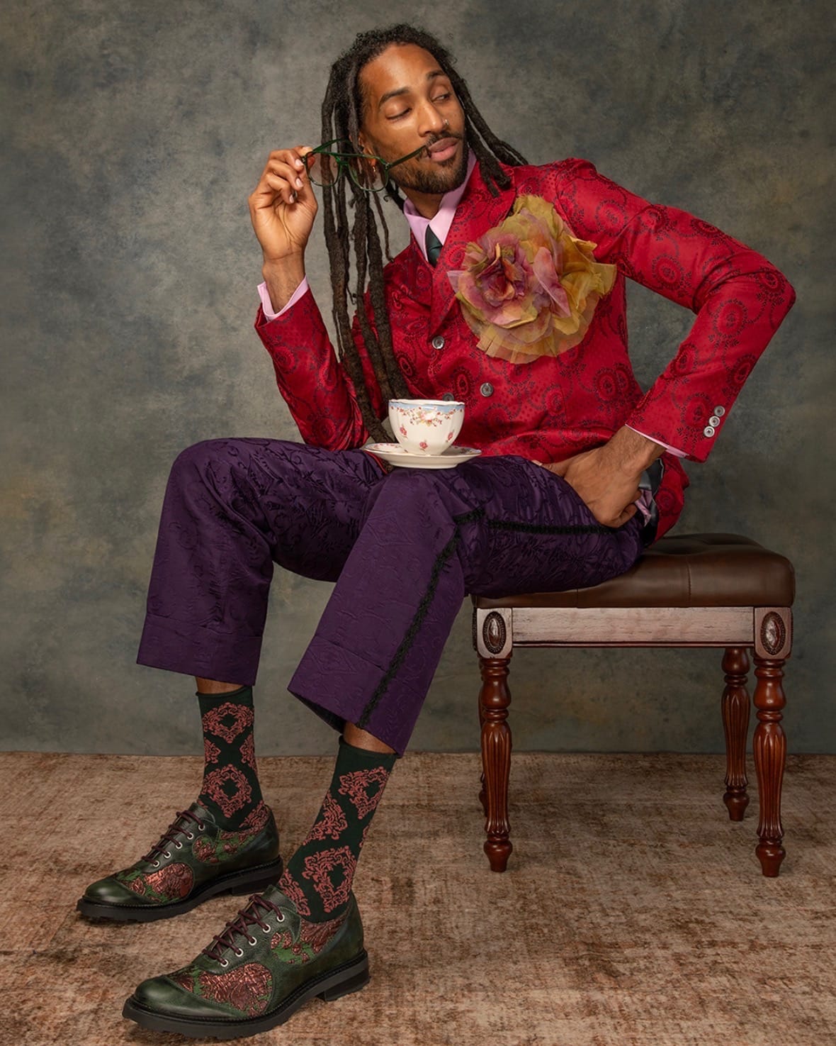 Greg Banks in a red brocade suit seated with a teacup