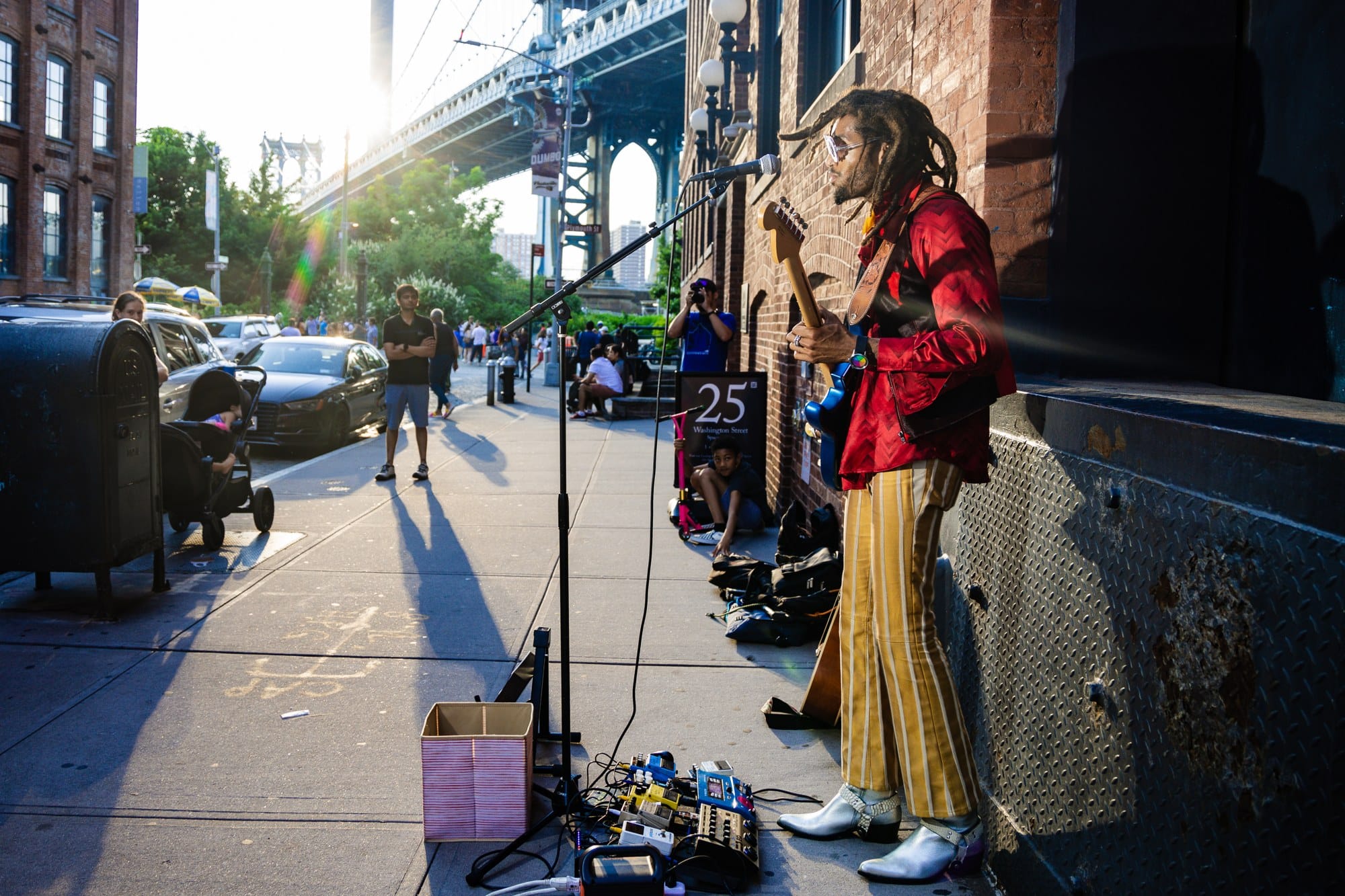 Greg Banks plays electric guitar on a Brooklyn sidewalk beneath the Manhattan Bridge