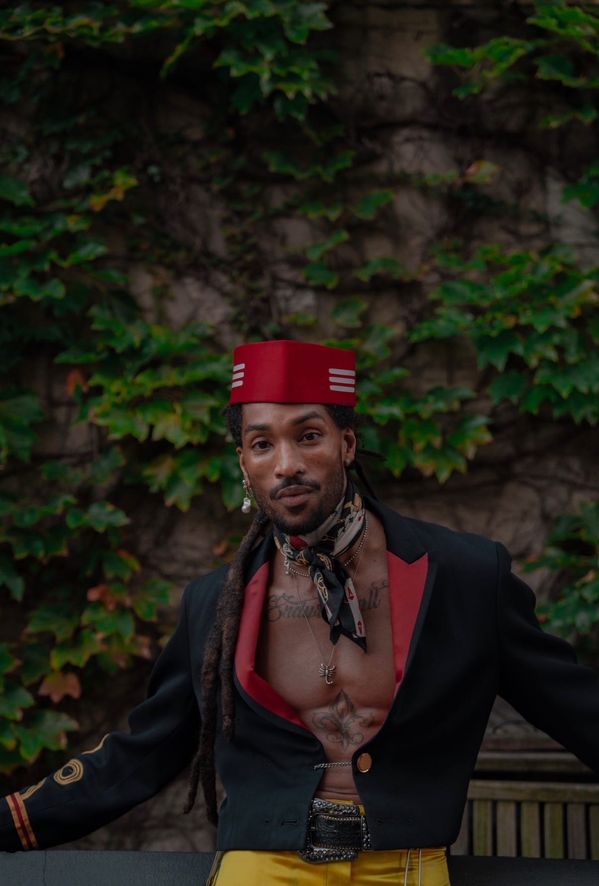 Greg Banks in a red cap and black blazer against an ivy wall